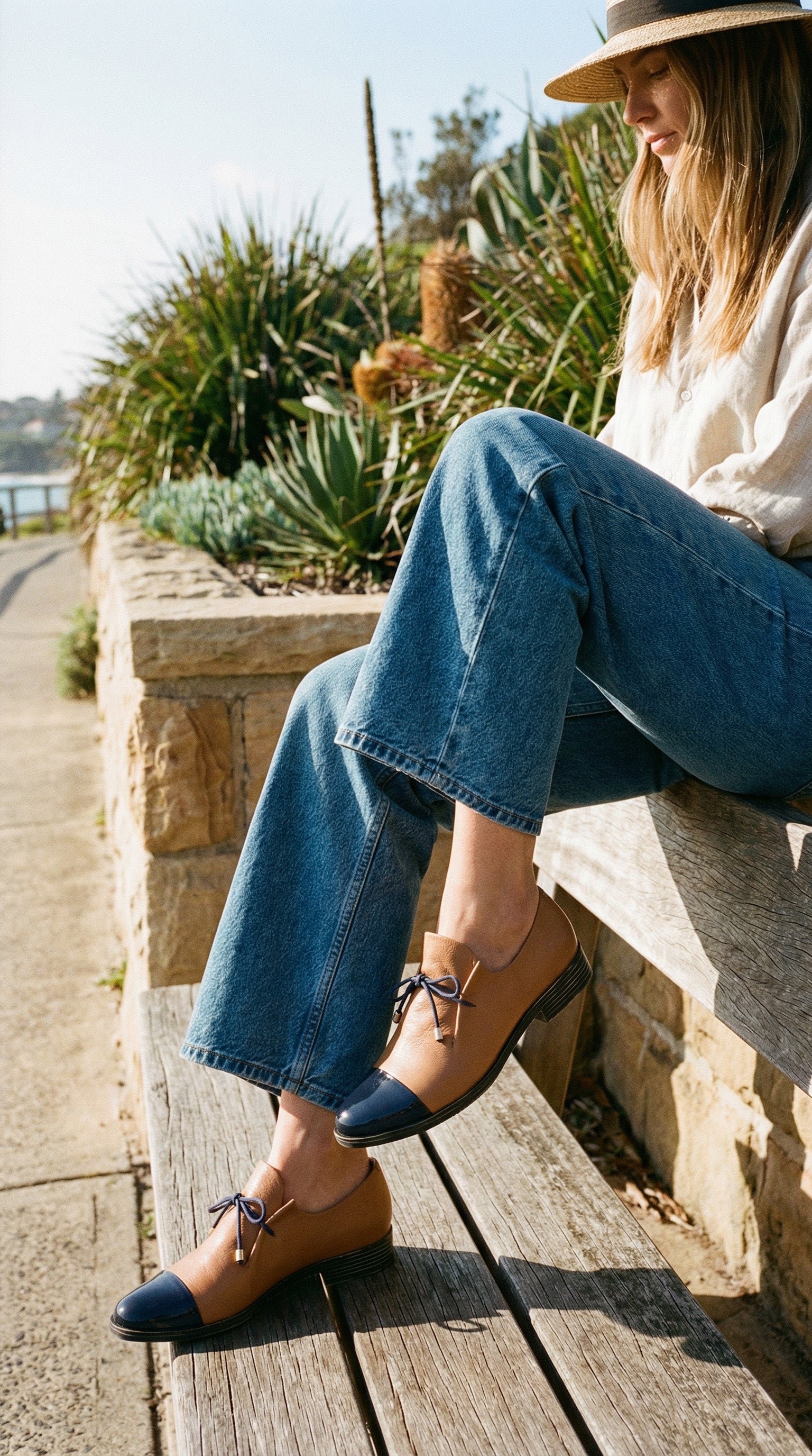 Woman sitting outdoors wearing blue jeans and brown shoes.